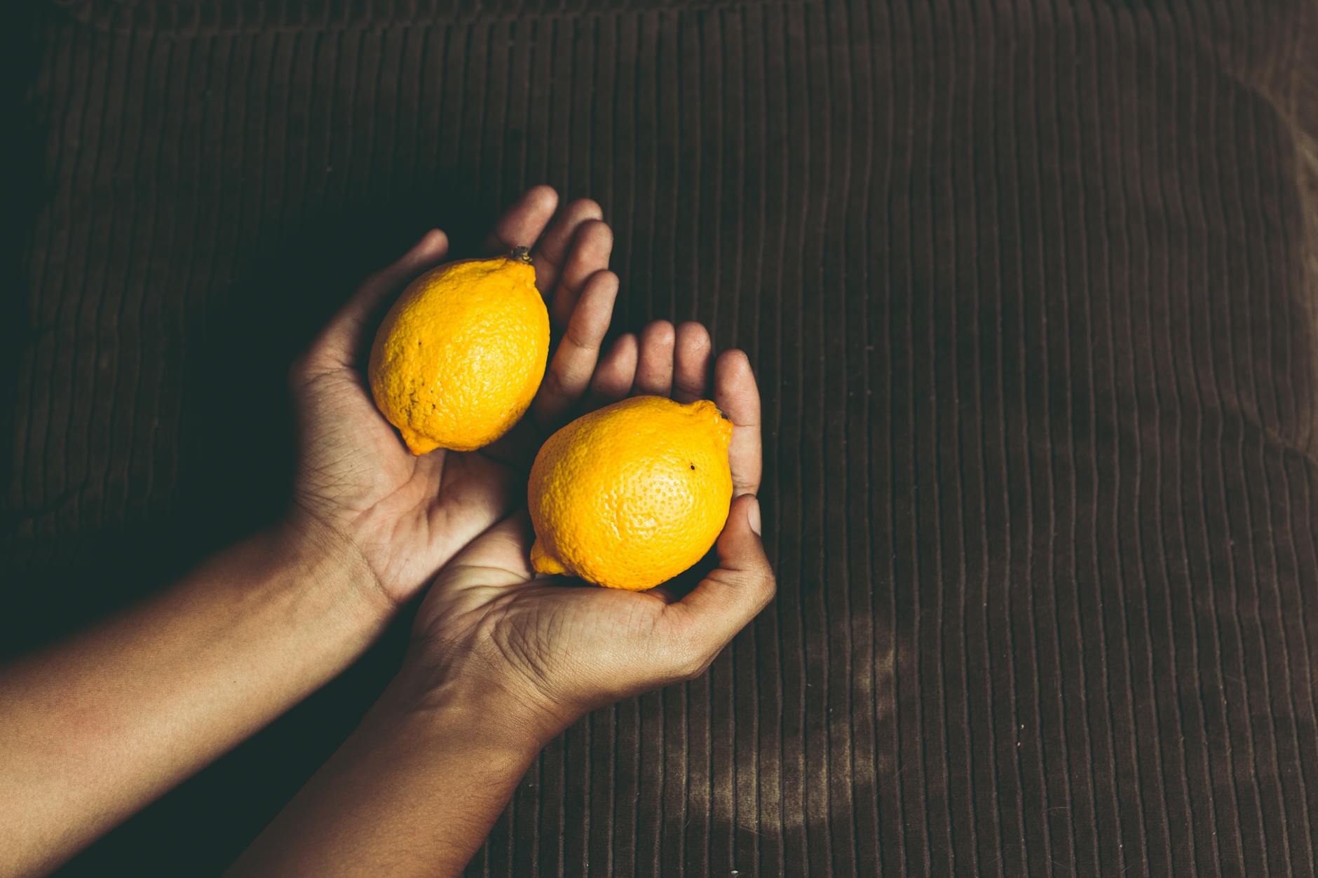 Hand with white nails holding a lemon on soft pink background surrounded by additional lemons