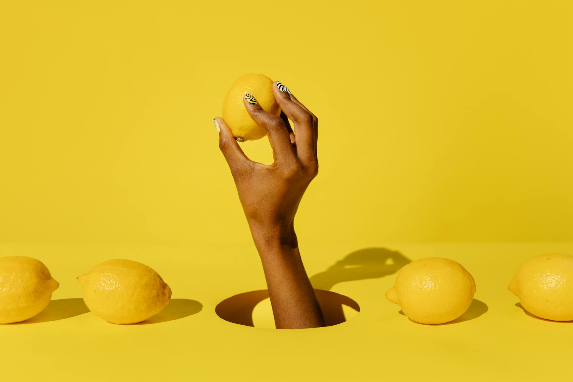 Hand holding a fresh lemon against a bright yellow background