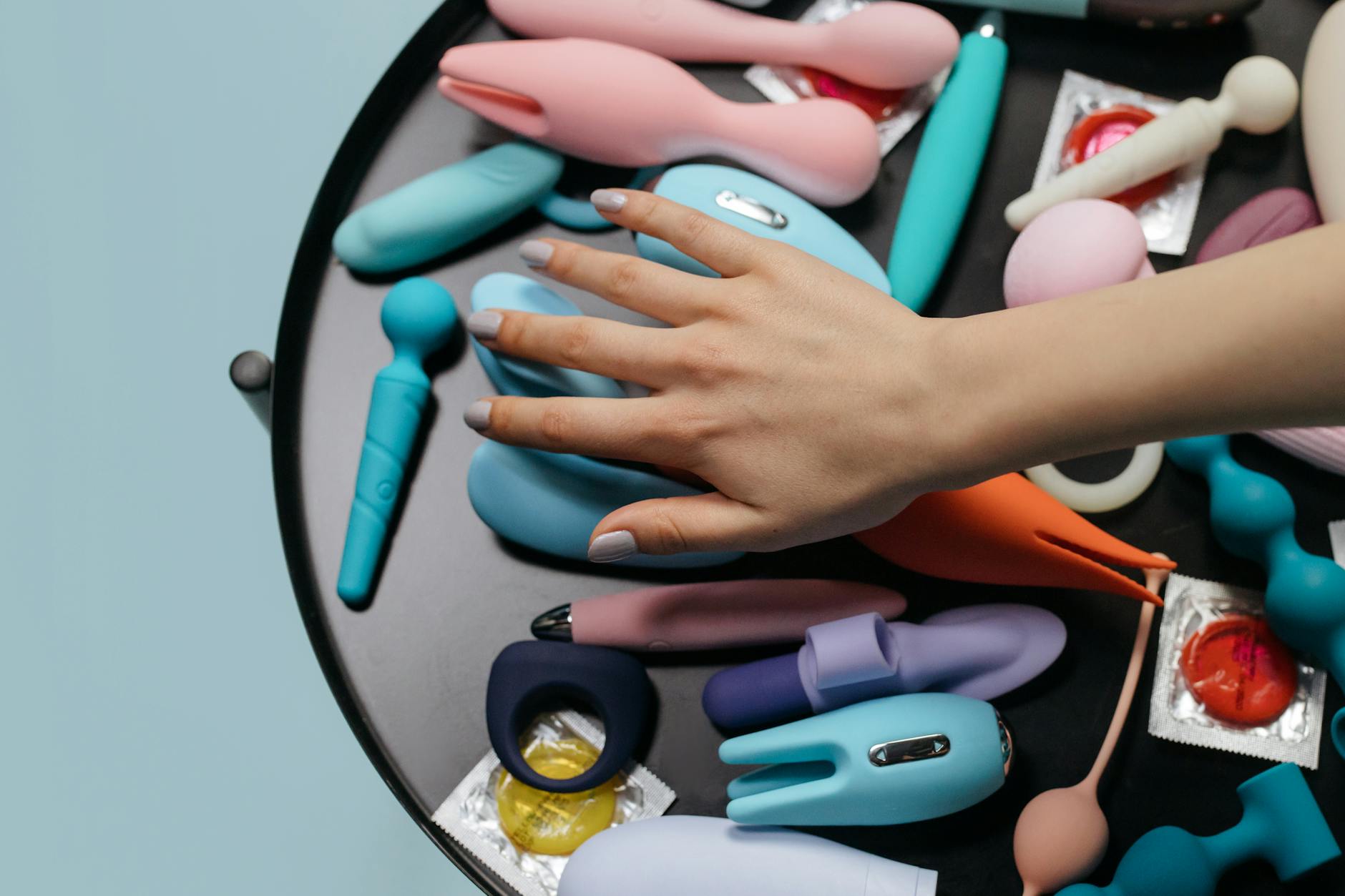 Hands holding a sleek blue vibrator against a purple background, illustrating intimate clitoral stimulation