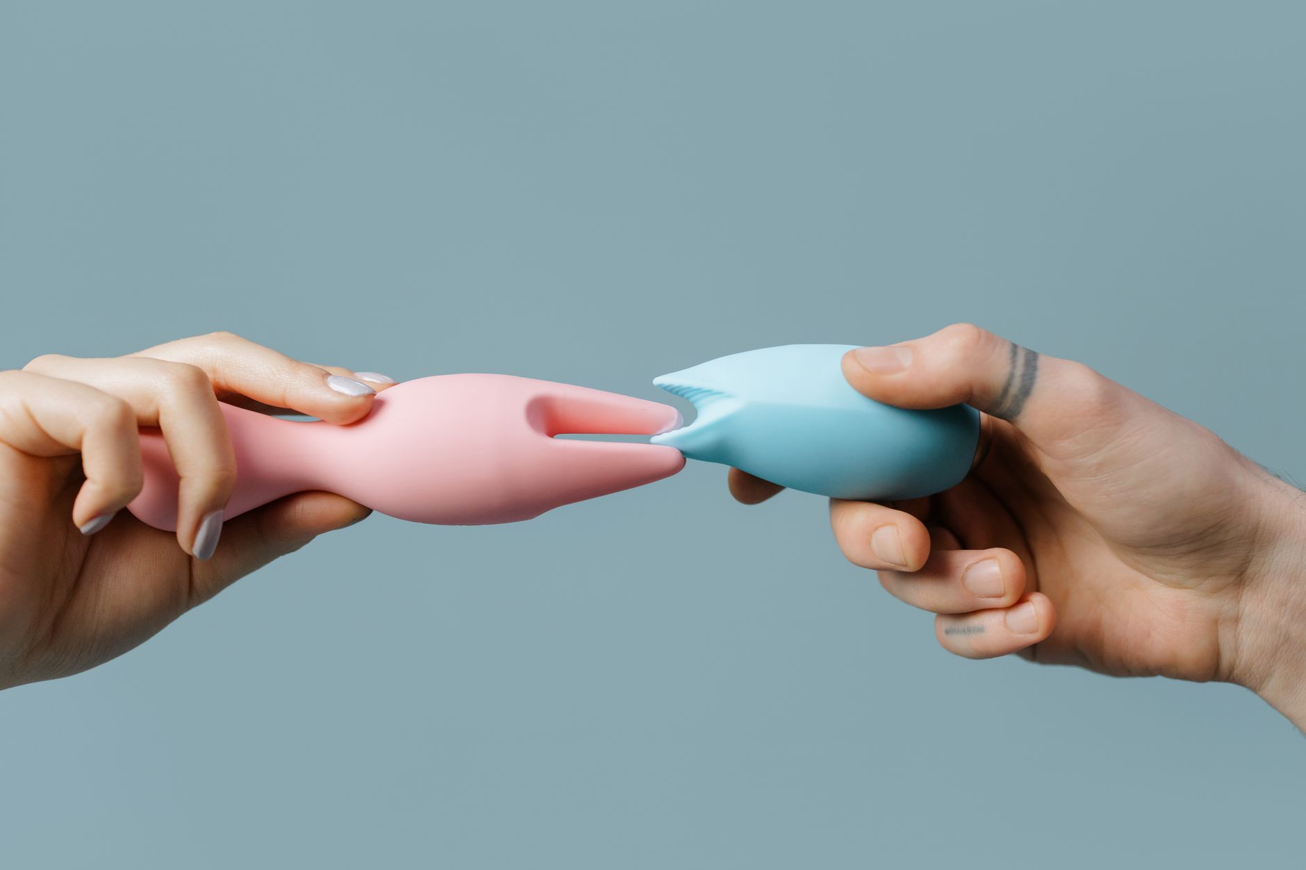 Hands holding pastel-colored silicone vibrators against a neutral background