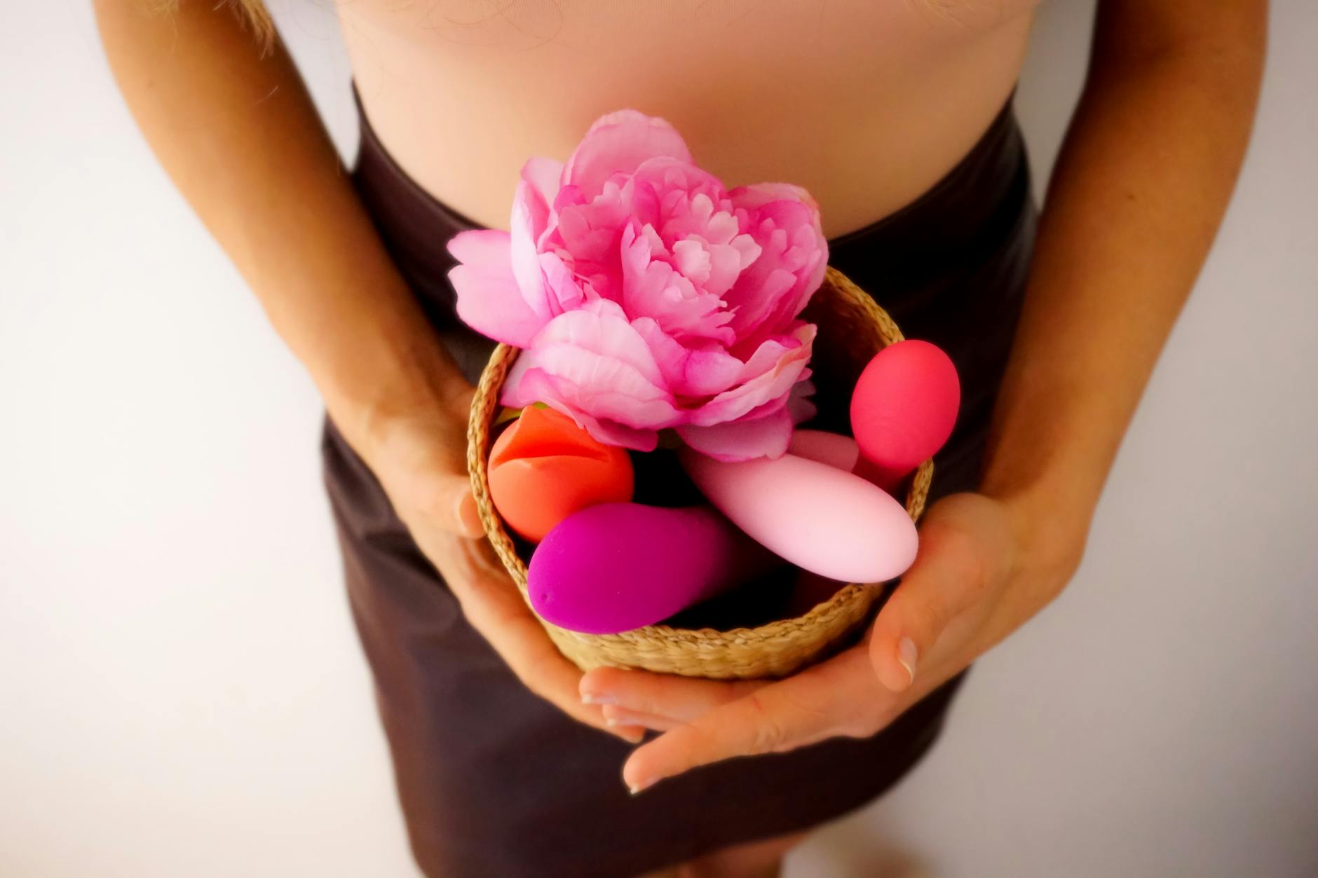 A person holding a basket containing colorful vibrators and fresh flowers, representing pleasure and self-care during high-stress periods